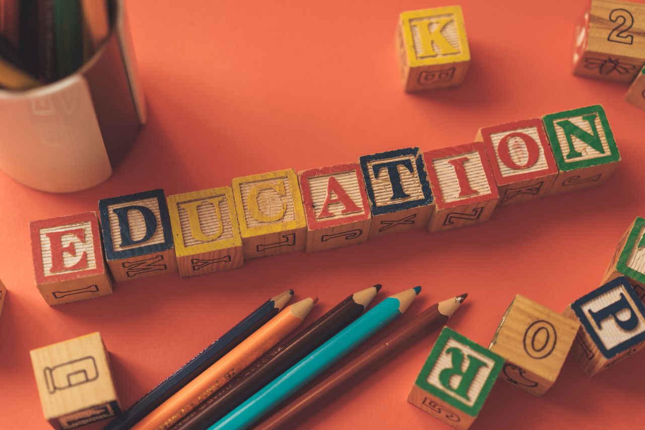Alphabet blocks spelling 'EDUCATION' on orange background with pencils.